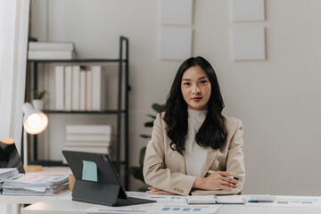 Confident and Composed: A professional businesswoman exudes confidence and composure as she leans against her desk in a modern office setting, ready to tackle any challenge. Her calm demeanor and focu