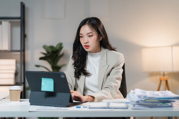 Focused in the Flow: A young Asian businesswoman diligently works late at her desk, illuminated by warm light, highlighting her dedication and ambition. 