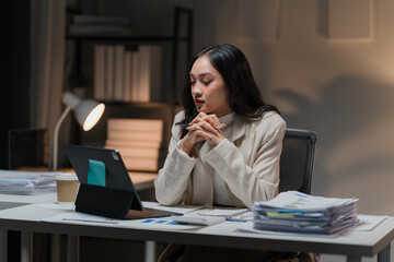 The Weight of Deadlines: A young Asian businesswoman, illuminated by the glow of her tablet, grapples with stress and fatigue as she works late into the night. 
