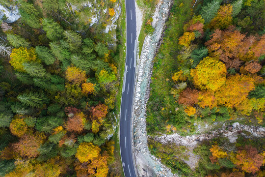 Aerial view of a vibrant autumn landscape with meandering roads and lush forests in a serene valley, Liezen, Austria.
