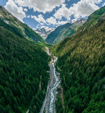 Aerial view of majestic mountains and a serene valley with a winding river surrounded by lush forest, Gran Paradiso National Park, Cogne, Italy.