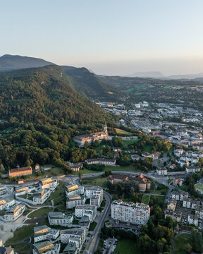 Aerial view of the beautiful historic cityscape featuring the Basilique de la Visitation surrounded by mountains and greenery at sunset, Annecy, France.