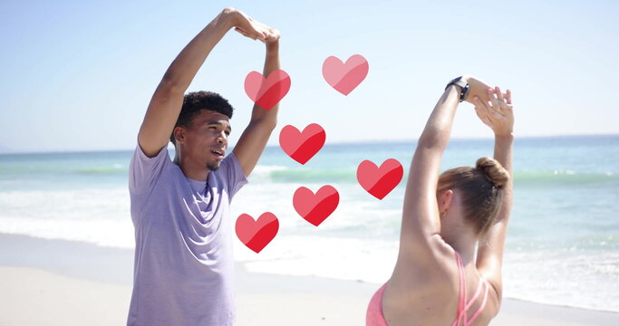 Image of red hearts over diverse couple stretching on beach