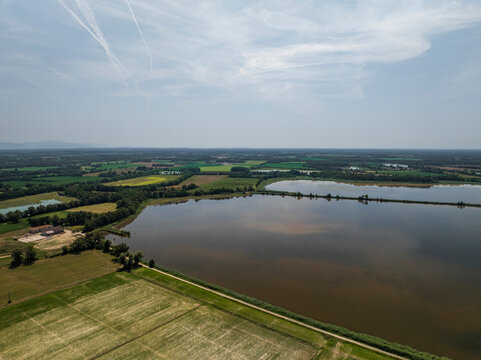 Aerial view of serene Parc des Oiseaux with tranquil lake and picturesque fields under a sunny sky, Marlieux, France.
