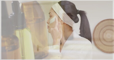 Image of dropper bottle of essential oil over happy biracial woman applying under eye mask