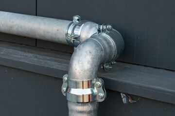 Metal plumbing pipe connection on a building wall in daylight