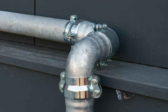 Metal plumbing pipe connection on a building wall in daylight