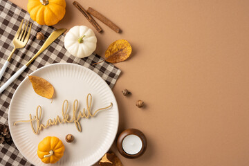 Top view of a Thanksgiving table setting featuring a 'thankful' plate, small pumpkins, autumn leaves, and cinnamon sticks, creating a festive and cozy atmosphere