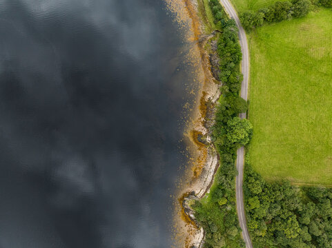 Aerial view of serene Loch Leven with a winding road and lush trees, Fort William, Scotland.
