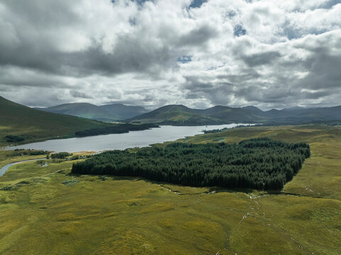 Aerial view of Loch Tulla surrounded by lush forests and majestic mountains under a cloudy sky, Bridge of Orchy, Scotland.