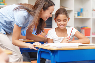 Education, advice and teacher with student in classroom for learning, knowledge and studying. Happy, helping and female educator talk to girl child for assistance in lesson at school for scholarship.