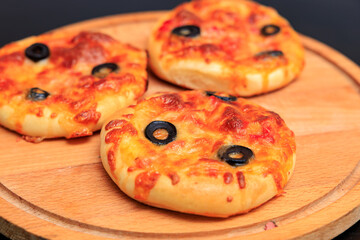 Three small pizzas with olives on top sit on a wooden cutting board