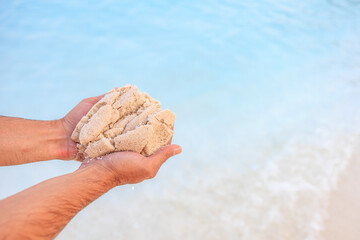 A person is holding a handful of sand on a beach