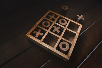 Tic Tac Toe game or OX game made of wooden blocks on wood table in the dark, there is a sense of seriousness.