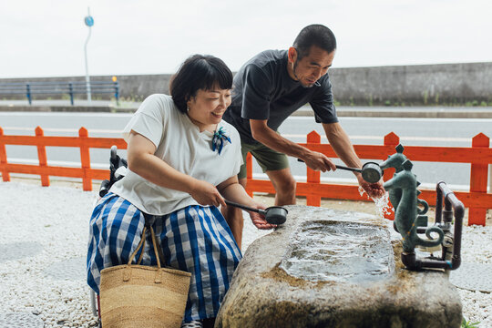 日本人の車椅子に乗った女性と彼氏が神社にお参りをするために手を清めている
