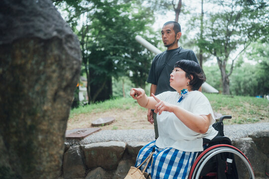 車椅子に乗った女性と彼氏が旅の途中で石碑を読んで会話をしている
