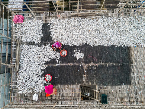 Aerial view of traditional fish processing with drying racks and people in a vibrant community, Chittagong, Bangladesh.