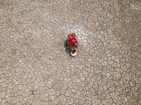 Aerial view of a woman collecting water in a drought-affected coastal village with cracked earth, Khulna, Bangladesh.