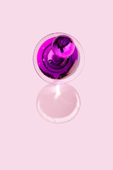 Disco ball on purple drink in glass with shadow on pink background. Top view.