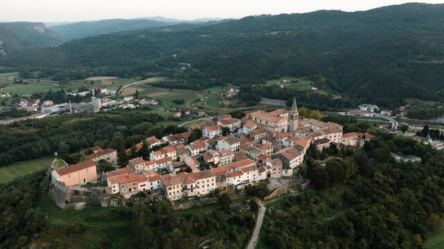 Aerial view of picturesque village with historic architecture and red roofs surrounded by serene hills and greenery, Buzet, Croatia.