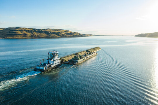 Aerial view of a river barge and tugboat on calm water with beautiful reflections, Columbia River Gorge, Benton County, United States.