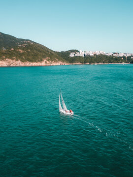 Aerial view of serene Chung Hom Kok beach with sailboats on the calm ocean and urban cityscape in the background, Southern District, Hong Kong.