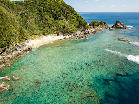 Aerial view of beautiful sandy beach with clear water and lush trees along the coast, Kunigami Son, Japan.