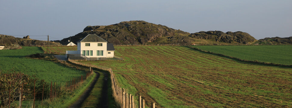 A white house surrounded by green meadows and fields, Rogaland, Norway.