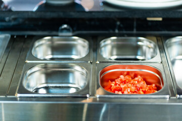Metal containers filled with various sliced vegetables and ingredients in a professional kitchen setting