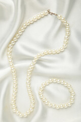 Pearl necklace with bracelet on white silk background. Top view