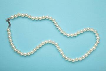 Elegant pearl necklace on blue background, top view. Space for text