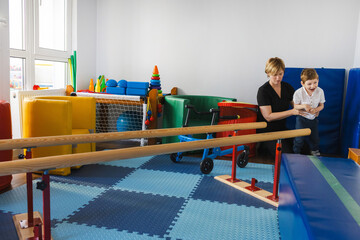Young boy is assisted by therapist in physical rehabilitation exercises in bright, playful therapy...