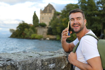 Fototapeta premium Handsome man making a phone call with the gorgeous Yvoire castle in the background 
