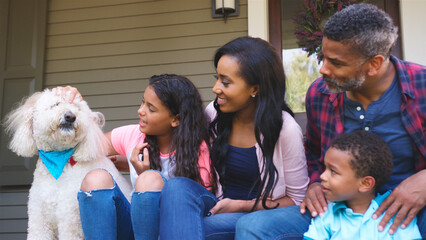 Family With Children And Pet Dog Sit On Steps Of Home