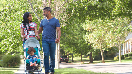 Couple Push Daughter In Stroller As They Walk Along Suburban Street