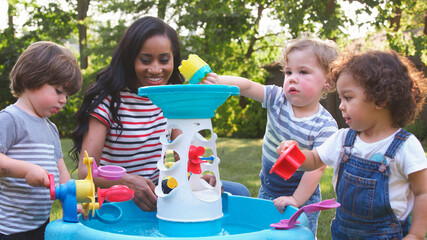 Mother And Young Children Playing With Water Table In Garden