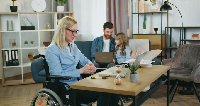 Handicapped woman has videocall on laptop handsome father sitting on the couch together with his cute teenage daughter