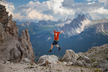 Young happy man high jumping on rocks in the Dolomite mountains.