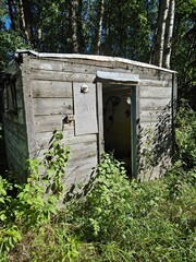 The exterior of a rustic, old, and weathered small wooden shed with an open doorway. 