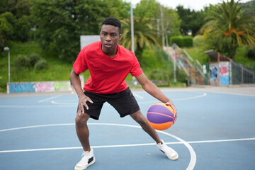 Obraz premium Young afro sportive man playing basketball outdoors