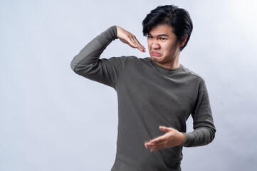 An Asian man in a gray long-sleeved shirt makes a disgusted expression while covering his mouth and...