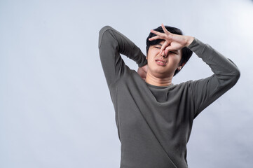 An Asian man in a gray long-sleeved shirt makes a disgusted expression while covering his mouth and...