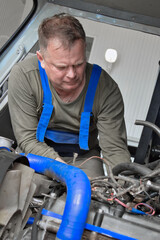 A mechanic is repairing an engine in a car repair shop. He carefully checks and adjusts the various...
