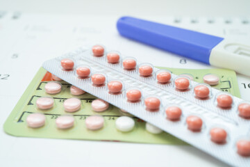 Pregnancy test and birth control pills on calendar, contraception health and medicine.