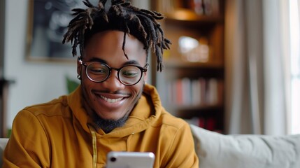 A young man in a hoodie engages in a friendly video call, smiling while seated on a couch in a bright, inviting living room