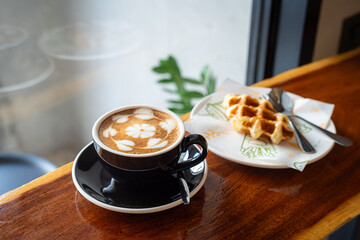 Hot coffee latte with latte art milk foam in cup mug and Homemade Belgian Waffles with honey on wood desk on top view. As breakfast In a coffee shop at the cafe,during business work.