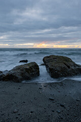 Two big rocks on the shore with cloudy sky.
