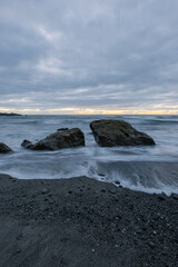 Two big rocks on the shore with cloudy sky.
