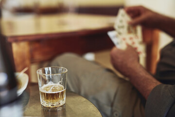Card game, drink and person hands in retirement with senior care, playing and fun on table. Cognitive, memory and activity in group with hobby, relax and poker for brain engagement and whiskey