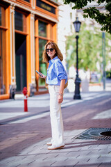 A middle-aged woman with blonde hair holding her smartphone in her hand and walking down the street